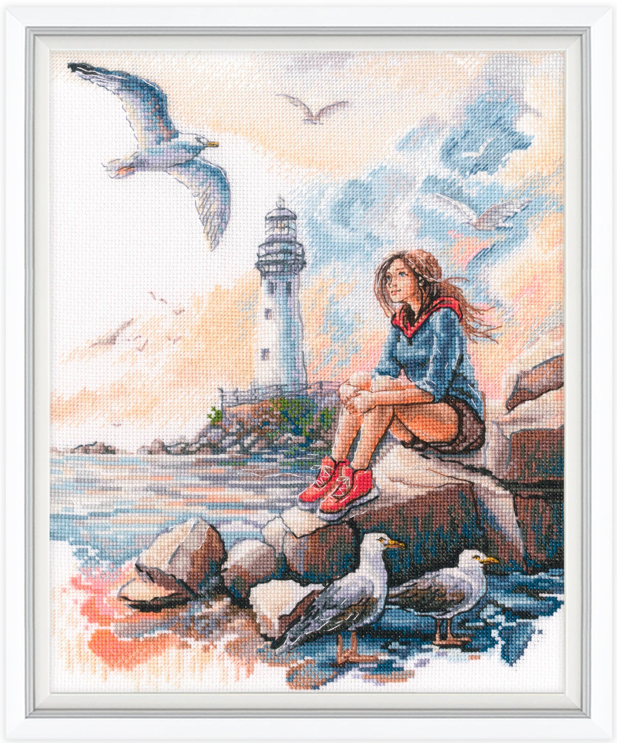 Cross-stitched artwork of a girl sitting on rocks by a lighthouse with seagulls.