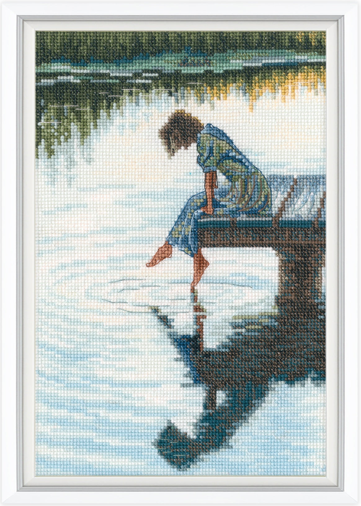 Cross-stitched artwork of a person sitting on a dock by a lake with reflections.